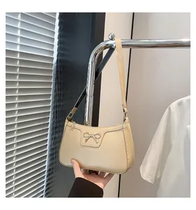 Close-up of beige leather baguette bag with metal bow detail and flower zipper charm