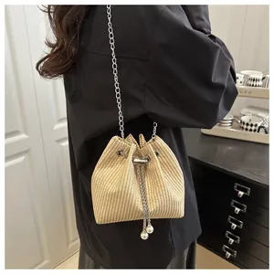 Detail of beige straw bucket bag with silver chain strap and pearl drawstring tassels