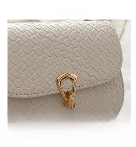 Close-up of woven texture and golden metal buckle on beige leather crossbody bag