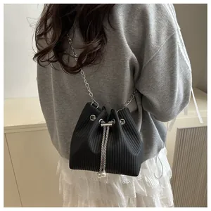 Detail of black drawstring bucket bag with woven texture, silver chain, and pearl charms