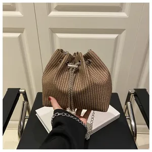 Close-up of woven bucket bag featuring metal chain strap and elegant pearl charm detail