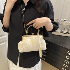 Close-up of beige floral jacquard shell bag with gold metal handle and silk tassel