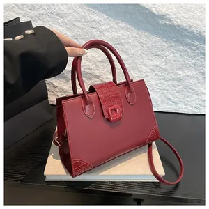Borsa quadrata rosso scuro con dettagli in pelle di coccodrillo su scrivania moderna