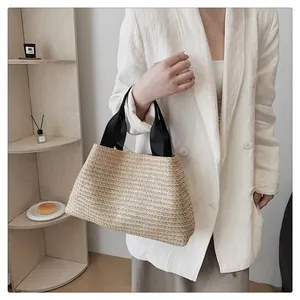 Detail of handwoven straw tote bag with black wide straps held by a model in a white blazer