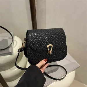 Elegant black woven texture crossbody bag with a golden metal buckle on a white pedestal