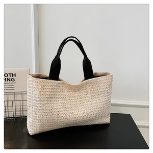 Detail of a beige woven straw tote bag with black canvas straps on a minimalist background