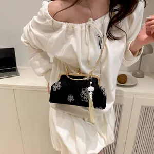 Detail of black velvet qipao bag with white flower embroidery and a gold chain strap