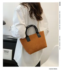 Detail of ginger corduroy tote bag with black handles and gold chain strap on model