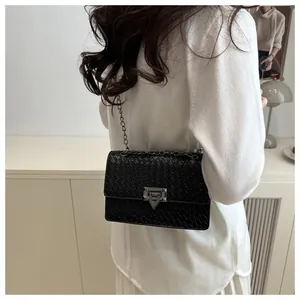 Detalle de bolso bandolera negro con patrón de piedra, hebilla plateada y correa de cadena