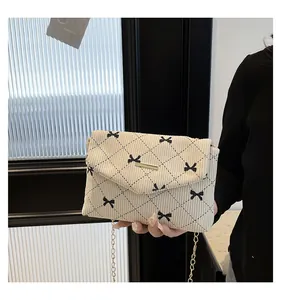 Close-up of cream corduroy crossbody bag with bow patterns and gold chain strap
