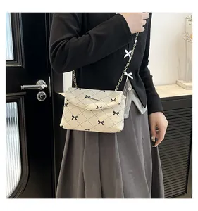 Detail of beige corduroy crossbody bag with quilted bow embroidery and gold chain strap