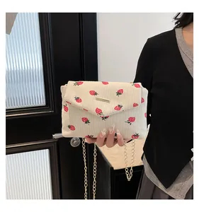 Corduroy shoulder bag with strawberry print and gold chain strap on a female model