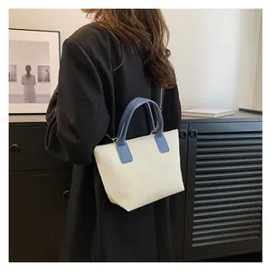 Detail of corduroy tote bag with blue leather handles worn over a black blazer