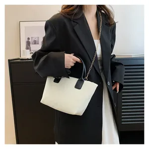 Detail of off-white corduroy tote bag featuring black handles and a gold metal chain strap