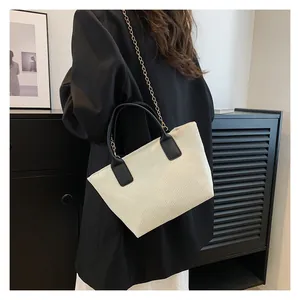 Detail of white corduroy tote bag with black leather handle and fine gold chain strap