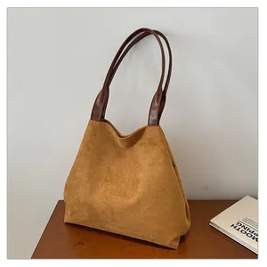Detail of the caramel suede tote bag with brown leather handles on a wooden table
