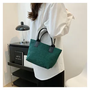 Detail of dark green corduroy tote bag with black leather handle and gold chain strap