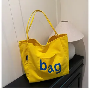 Détail d'un cabas en toile jaune montrant l'étiquette latérale et la poche avant
