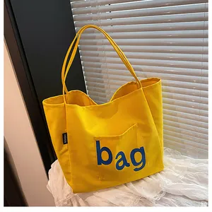 Détail du sac fourre-tout en toile jaune avec poche externe et lettrage bleu bag