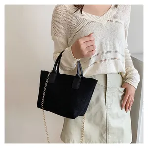 Detail of black corduroy tote bag showing vertical texture and gold chain strap on model
