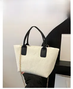 Detail of cream corduroy tote bag with black leather handles and golden metal chain