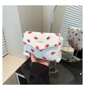 Detail of cream corduroy strawberry print bag with golden chain strap and flip cover