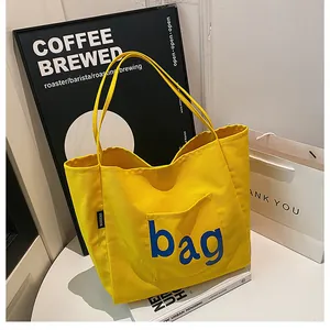Détail du sac fourre-tout en toile jaune avec impression de lettres bleues et étiquette