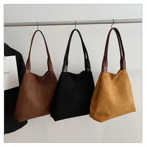 Three suede tote bags in brown, black, and yellow displayed on a hanging rack