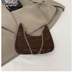 Dettaglio borsa a mezzaluna marrone con trama a serpente e catena dorata su blazer