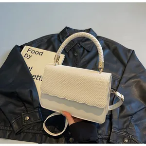 Détail du rabat à texture tissée blanche et quincaillerie dorée sur ce sac élégant