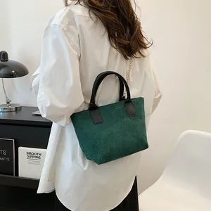 Green corduroy tote bag with black leather handles and gold chain strap on model