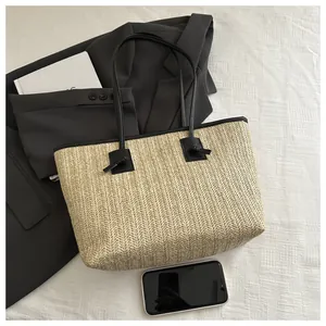 Detail of handwoven beige straw tote bag with black straps and large capacity for travel