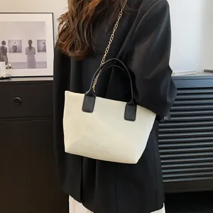 Minimalist beige corduroy tote bag with black handles and gold chain strap shown on model