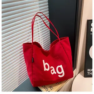 Détail d'un sac cabas en toile rouge avec lettrage blanc et étiquette latérale mode