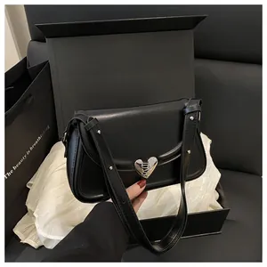 Dettaglio di una borsa a tracolla in pelle nera con chiusura a cuore argento in una scatola