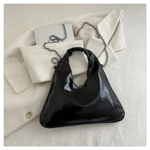 Detail einer glänzenden schwarzen asymmetrischen Handtasche mit silberner Metallkette