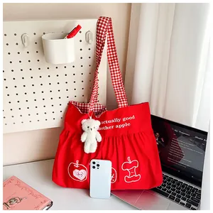 Detail of red canvas travel tote with apple print, checkered strap, and bear keychain