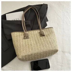 Detail of hand-woven straw tote bag with brown leather trim and knotted shoulder straps