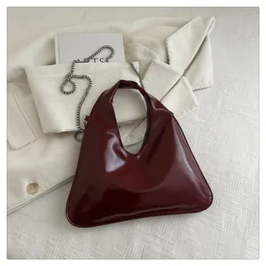 Detail der weinroten Lackhandtasche mit Silberkette auf strukturiertem Hintergrund