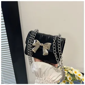 Detail of mini black patent leather crossbody bag featuring a large silver bow and chain