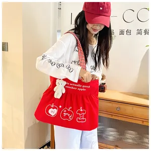 Detail of red canvas tote bag with apple print, plaid strap and cute plush bear charm