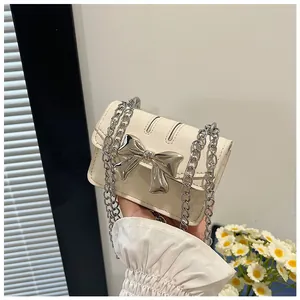 Detail of mini cream crossbody bag featuring a large silver bow and elegant chain strap