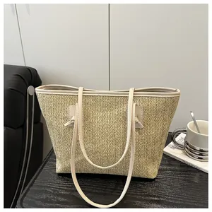 Detail of hand-woven straw tote bag with beige leather straps on a dark wooden surface