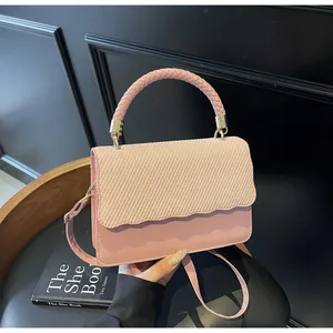 Détail du sac bandoulière rose avec poignée tressée et rabat texturé à bords ondulés