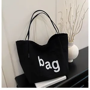 Détail d'un sac cabas noir en toile avec imprimé 'bag' blanc et une poche extérieure
