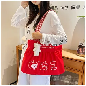 Detail of red travel tote with apple prints, checkered strap and plush bear charm