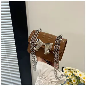 Detail of a mini brown leather crossbody bag featuring a large silver metal bow accent