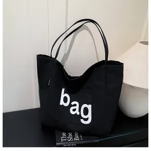 Détail du sac fourre-tout en toile noire avec lettrage blanc et étiquette mode