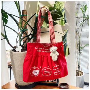 Detail of red travel tote with ruffled hem, plaid handles and cute bear charm