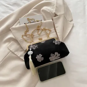 Close-up of black velvet evening bag with floral embroidery, gold handle and tassels
